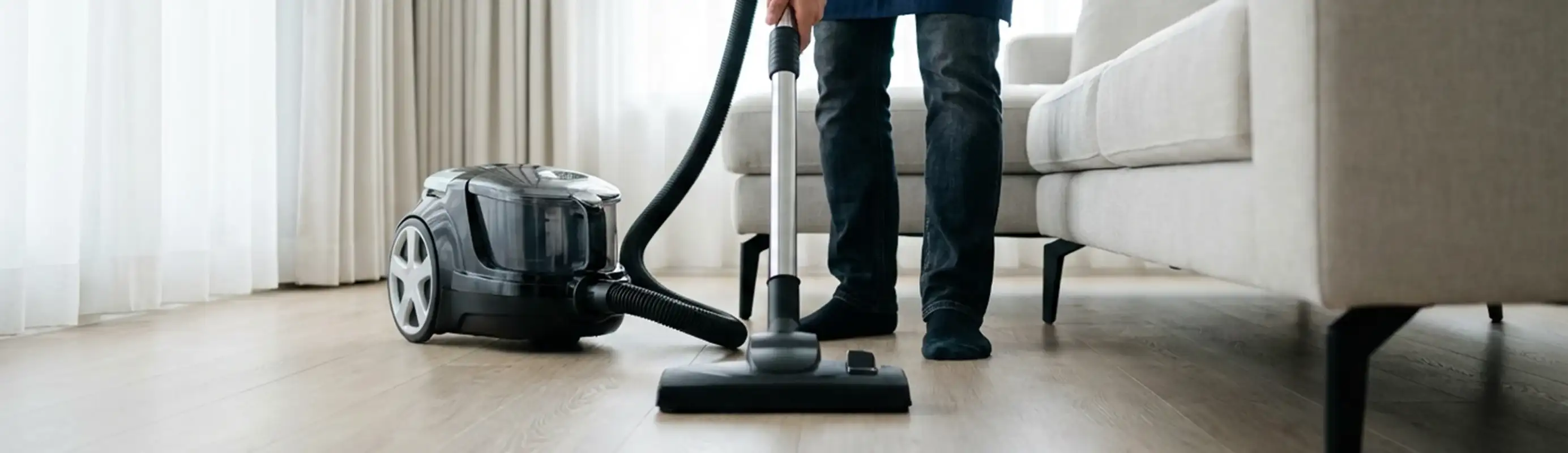 Professional house cleaner vacuuming a living room floor with a canister vacuum cleaner, Sioux Falls, SD.
