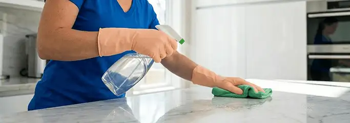 Maid service worker spraying and wiping a kitchen countertop with a microfiber cloth for sanitizing, Sioux Falls, SD.