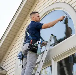 Professional window cleaner on a ladder using a squeegee to clean an exterior arched window, Sioux Falls, SD.