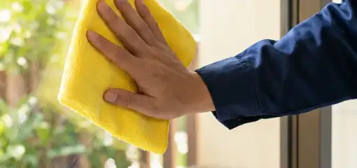 House cleaner wiping a glass window with a yellow microfiber cloth for streak-free cleaning, Sioux Falls, SD.